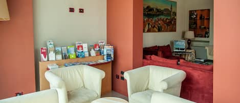 A living room with white leather sofas, a coffee table, a bookshelf with travel books, and a painting on the wall.