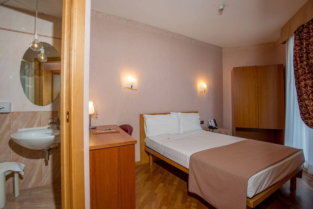 A bedroom with a wooden bed, a bedside table, a mirror, and a wardrobe.