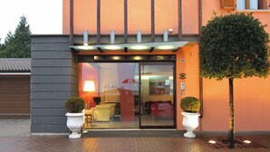 A hotel entrance with a glass door, two potted plants, and a lamp outside. - Sirio Hotel (Dormelletto)