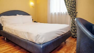 Una cama bien hecha con sábanas blancas, cabecera oscura y suelo de madera.