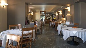 A restaurant with multiple tables and chairs, a stone floor, and warm lighting. - Sirio Hotel (Dormelletto)