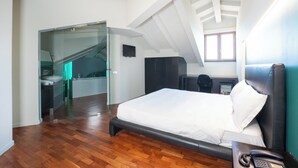 A modern bedroom with a large bed, a desk with a telephone, and a glass door leading to a bathroom. - Sirio Hotel (Dormelletto)