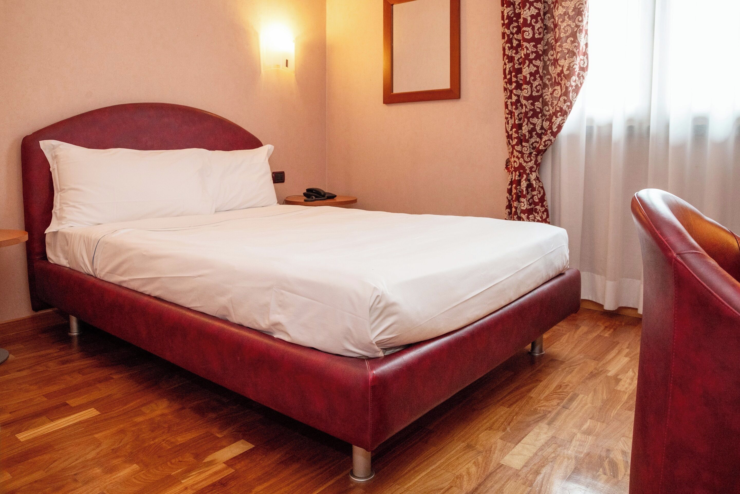 Ein Hotelzimmer mit einem roten Bett, Holzboden, einem Nachttisch mit Telefon und einem Sessel.