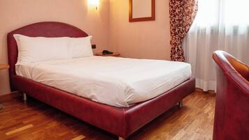 Ein Hotelzimmer mit einem roten Bett, Holzboden, einem Nachttisch mit Telefon und einem Sessel.