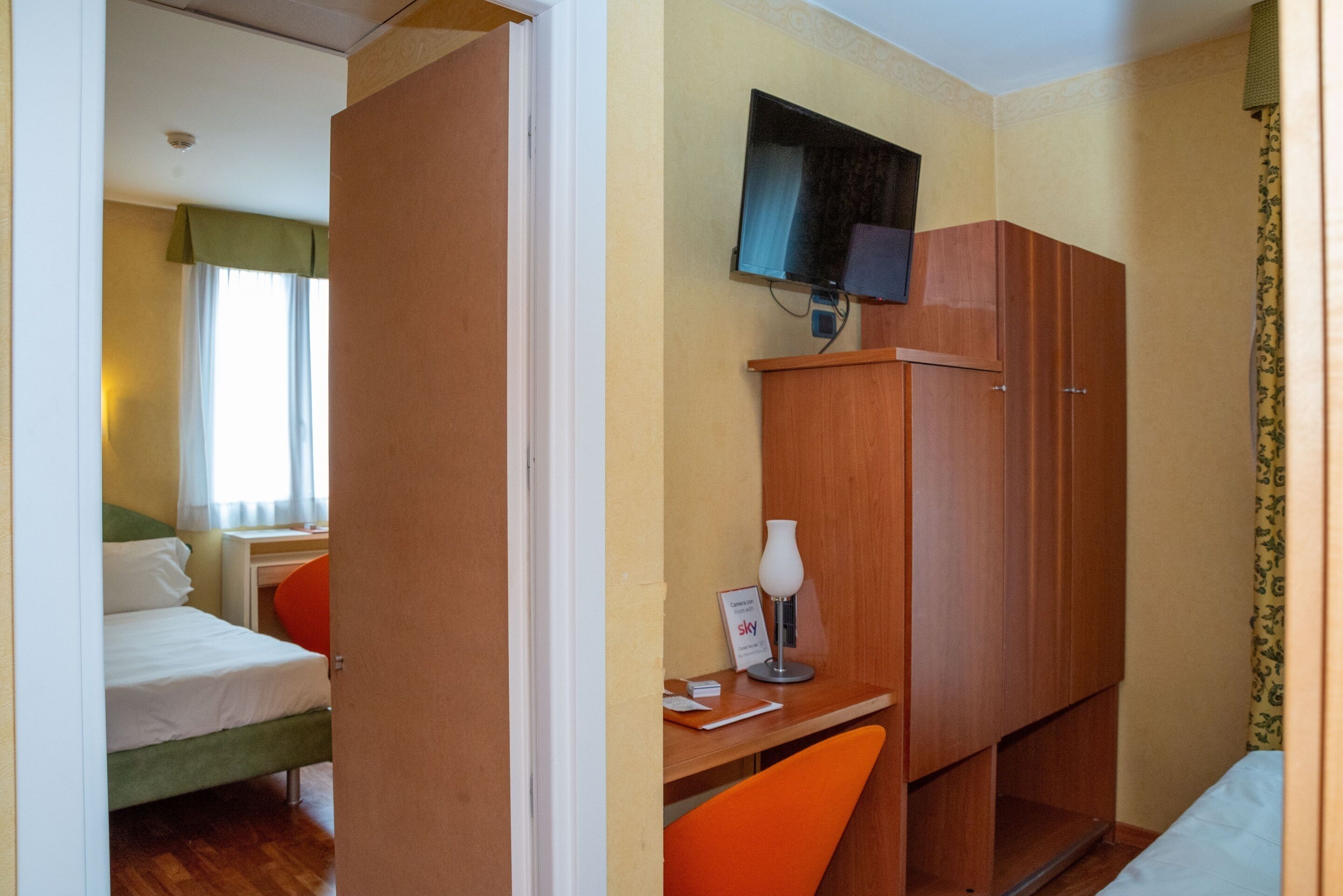 Een hotelkamer met een bed, een bureau met stoel, een televisietoestel en een kledingkast.