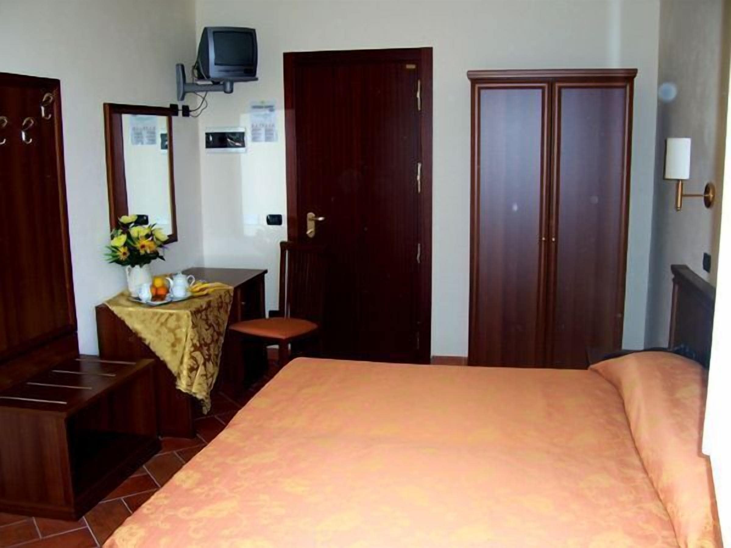 A bedroom with a bed, a desk with a chair, a dresser, and a television mounted on the wall.