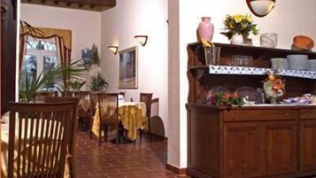 A dining area with brick flooring, wooden chairs, a table with a yellow tablecloth, and a wooden buffet with decorative items.