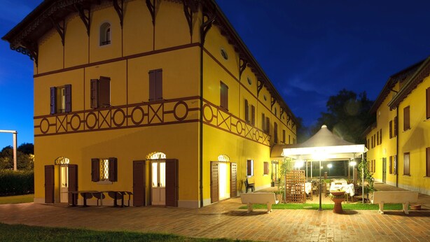 A yellow building with a covered patio area, benches, and a table with a white tablecloth. - Corte degli Estensi (Formigine)