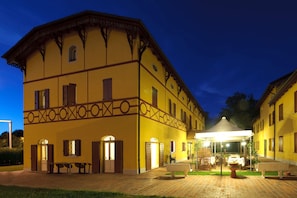 A yellow building with a covered patio area, benches, and a table with a white tablecloth.