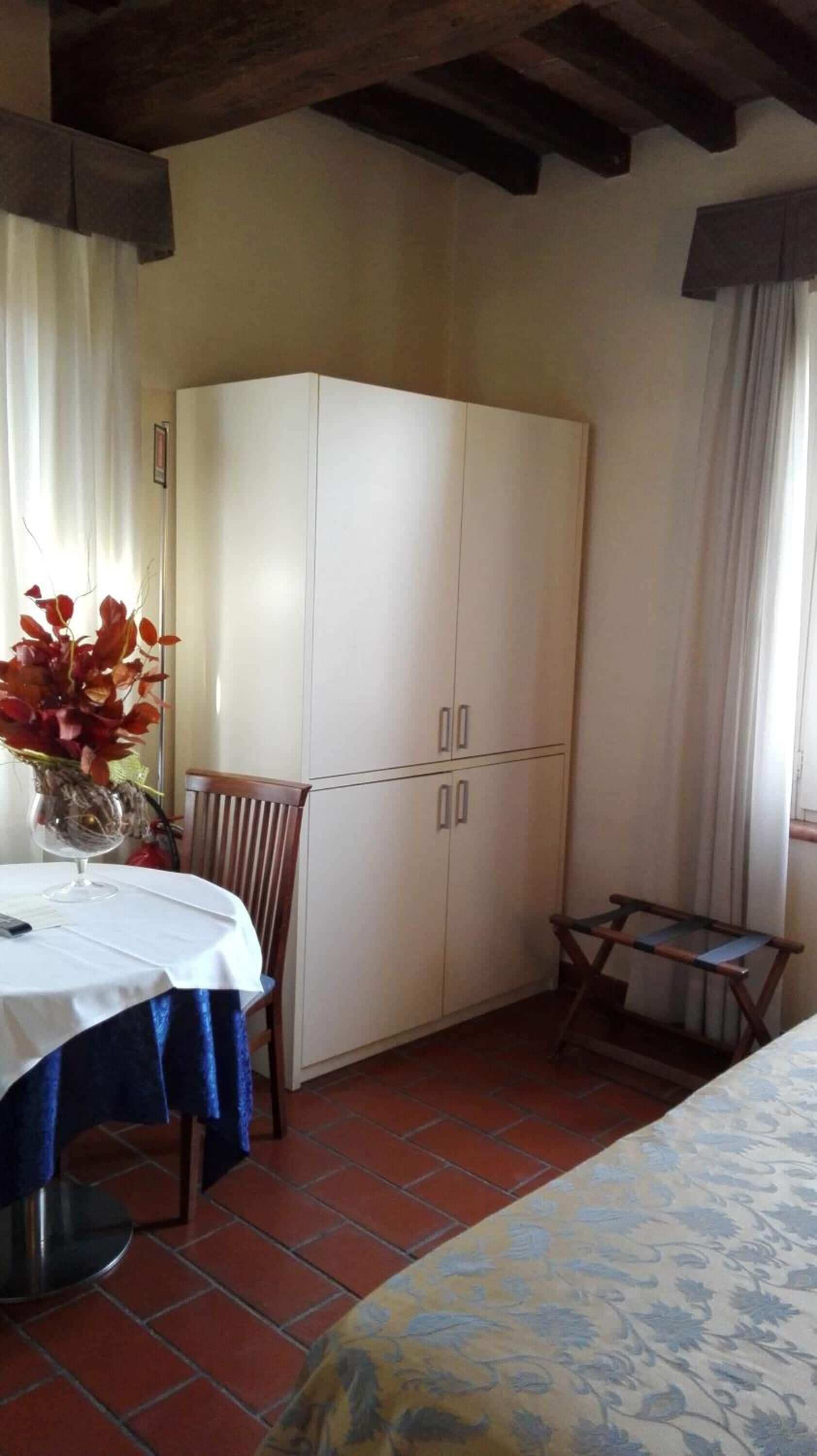 A room with a bed, a table with a vase of flowers, a chair, a wardrobe, and a window with curtains.
