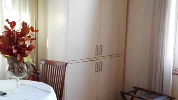 A room with a bed, a table with a vase of flowers, a chair, a wardrobe, and a window with curtains.