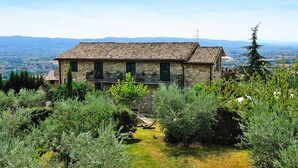 Un bâtiment en pierre, doté d’un toit en tuiles, entouré de verdure et offrant une vue sur un paysage lointain.