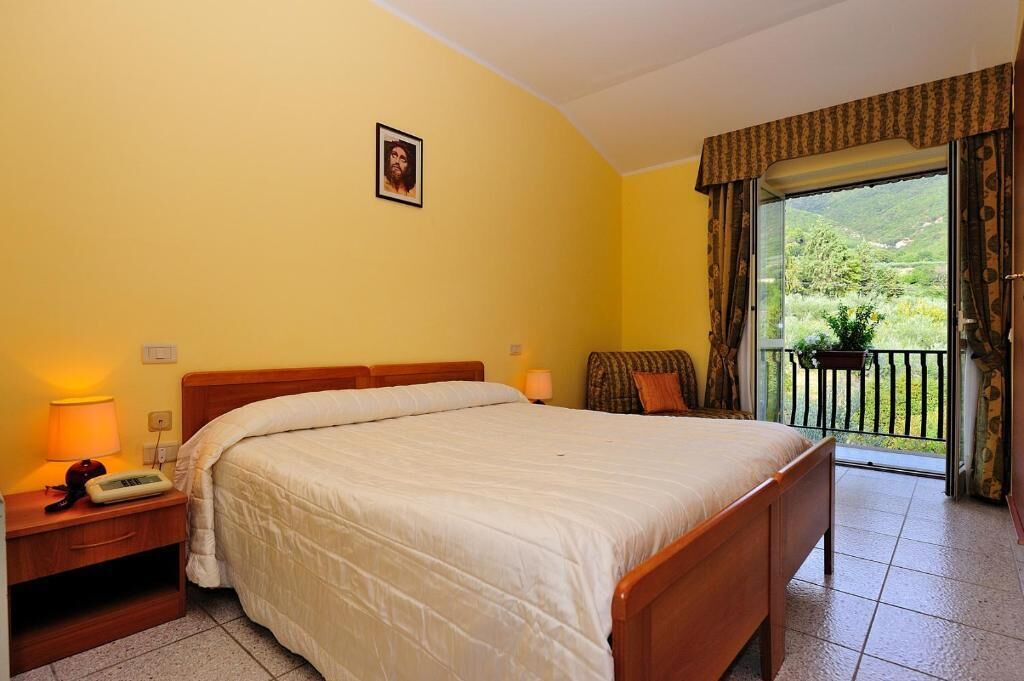 A bedroom with a bed, bedside table, lamp, and a view of a balcony with a railing.