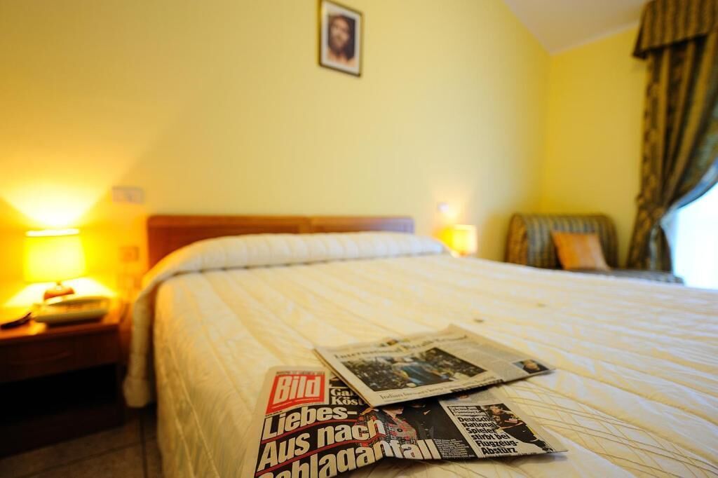 Una camera d'albergo con un letto, un comodino e una lampada.