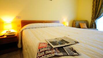 Una camera d'albergo con un letto, un comodino e una lampada.