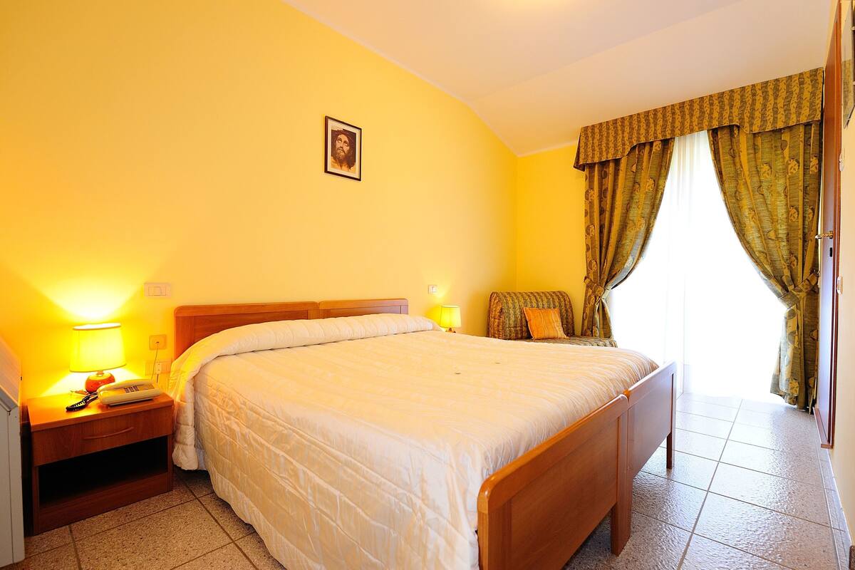 Una habitación de hotel con cama, mesita de noche, lámpara y cortinas.