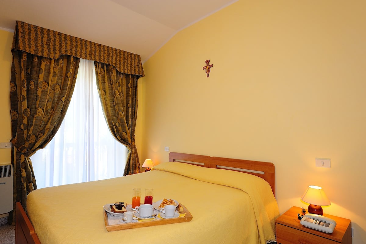 Habitación de hotel con cama, bandeja de desayuno, lámpara y una cruz en la pared.