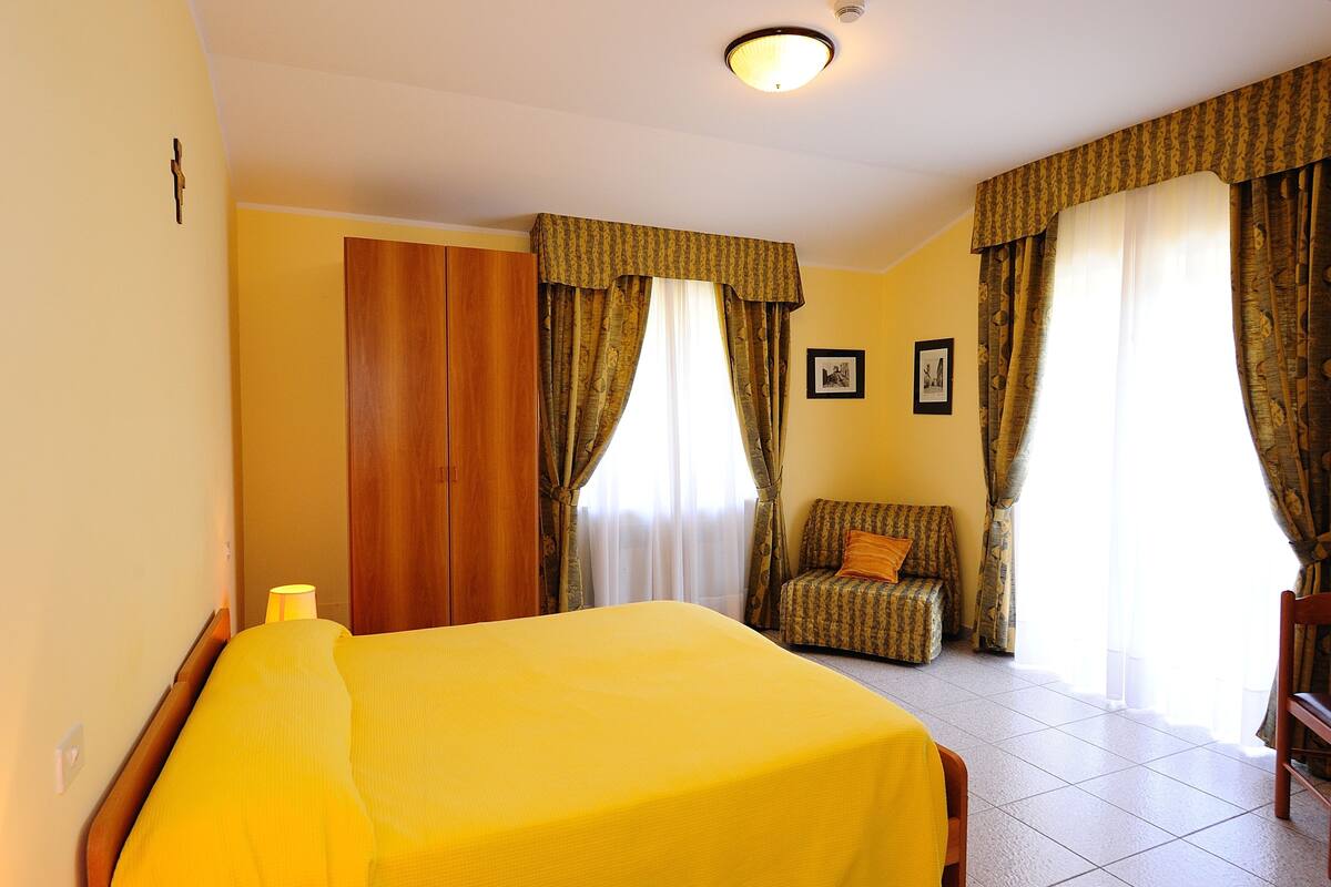 Una habitación de hotel con cama, una silla, un armario de madera y cortinas.