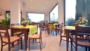 Un vaste espace dédié à la salle à manger, avec de nombreuses tables et chaises, de grandes fenêtres offrant une vue sur les arbres et un bâtiment situé au loin.