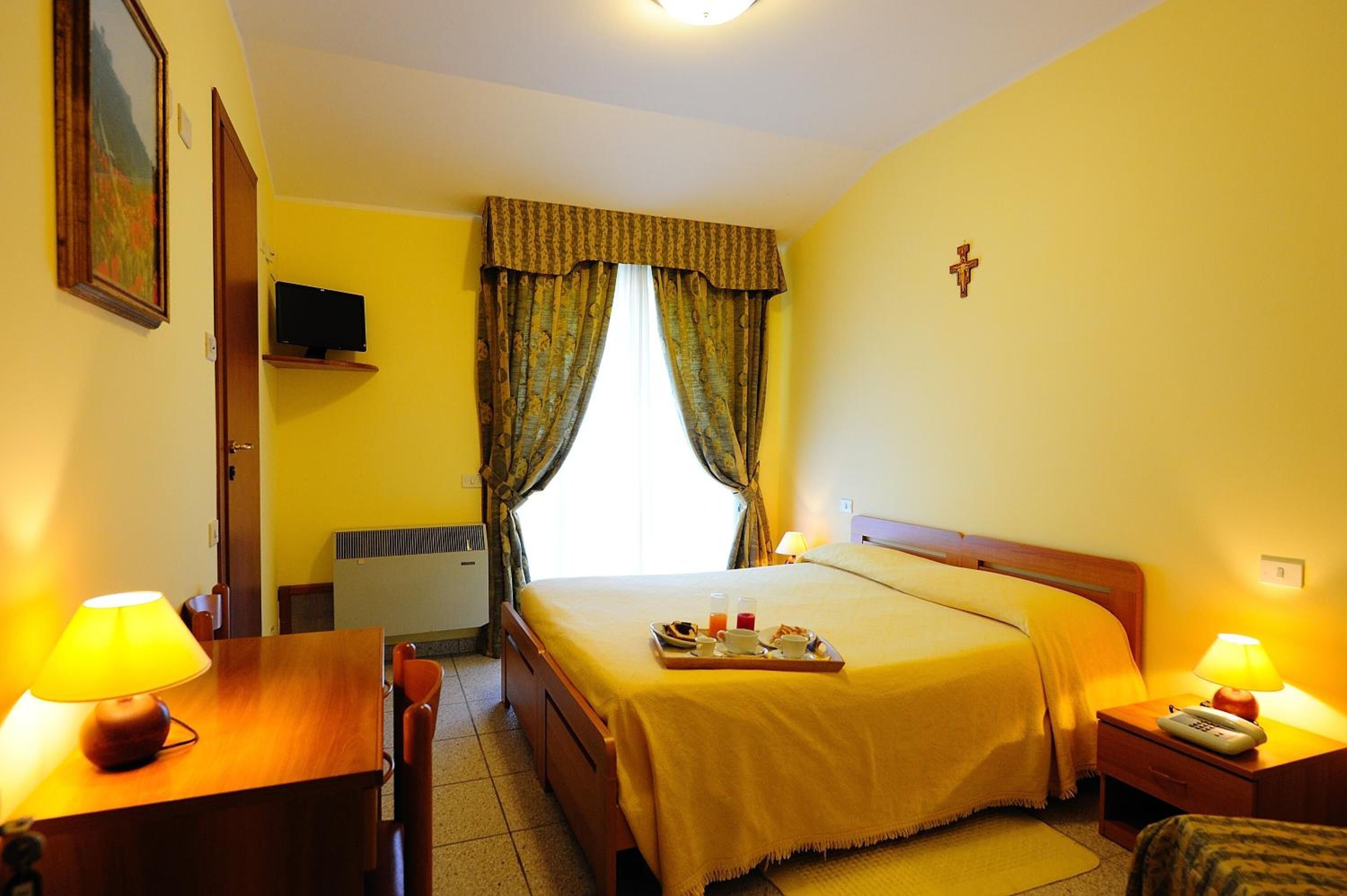 A hotel room with a bed, bedside table, lamp, and a tray with breakfast items.