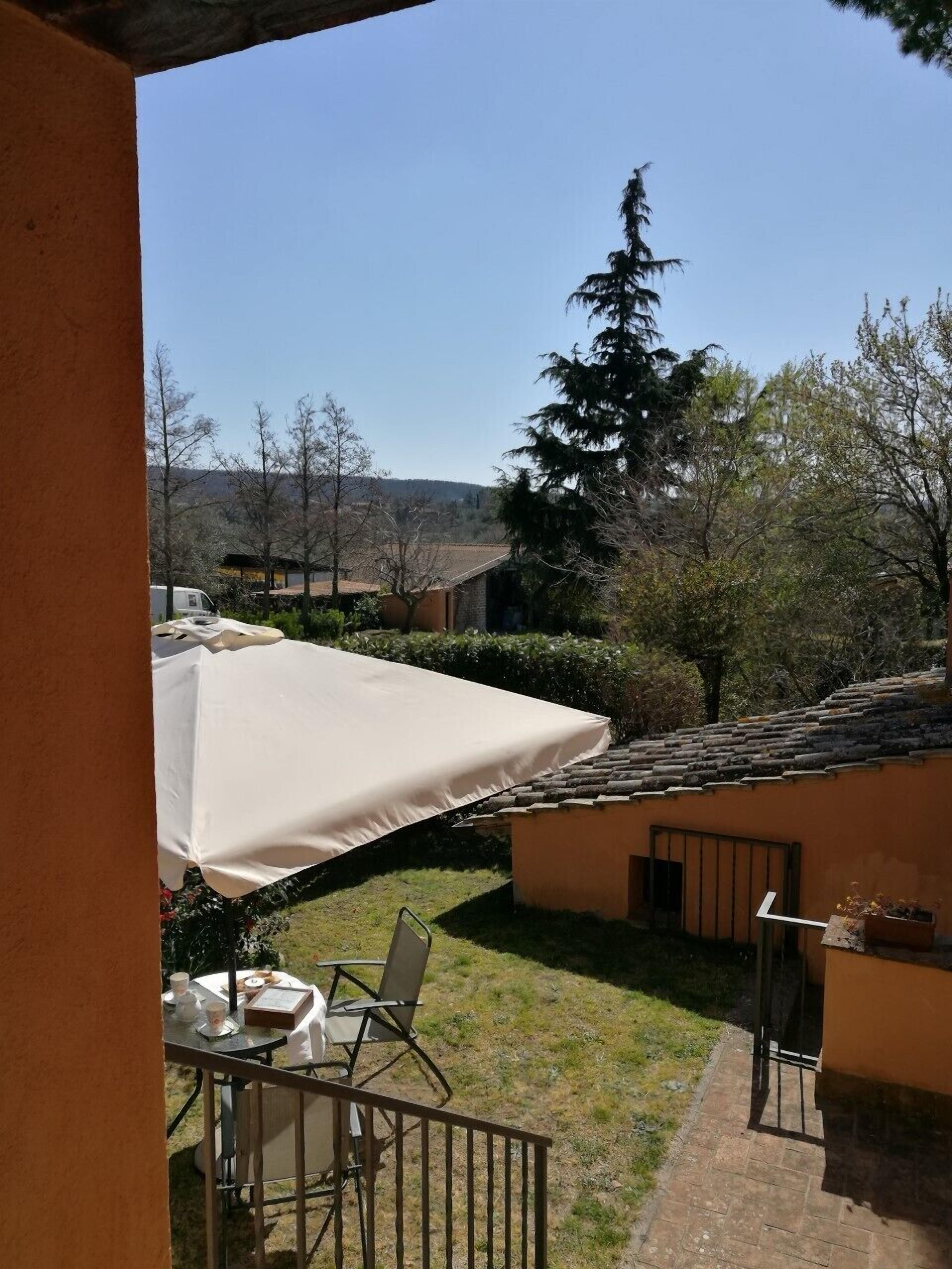 A patio area with a table and chairs, a large umbrella, and a view of a residential neighborhood with houses and trees.