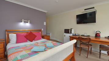 A bedroom with a bed, a desk, a TV, and a microwave.