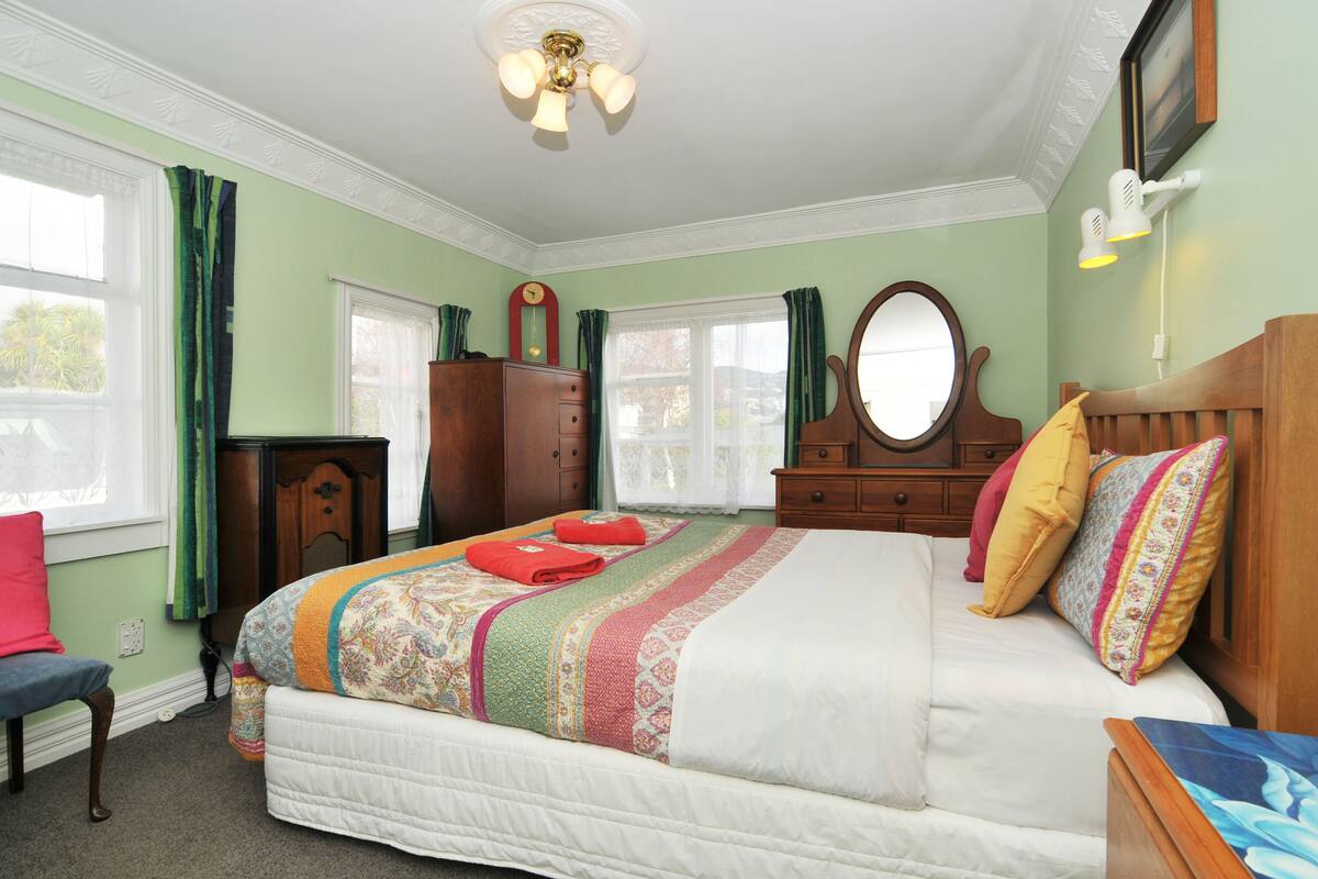 Une chambre à coucher avec un grand lit, une commode en bois, un miroir et une fenêtre avec des rideaux.