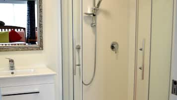 Un baño moderno con ducha de vidrio, tocador blanco con espejo y piso de madera.
