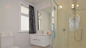 Een badkamer met een toilet, een wastafel, een spiegel en een douche met glazen wanden.