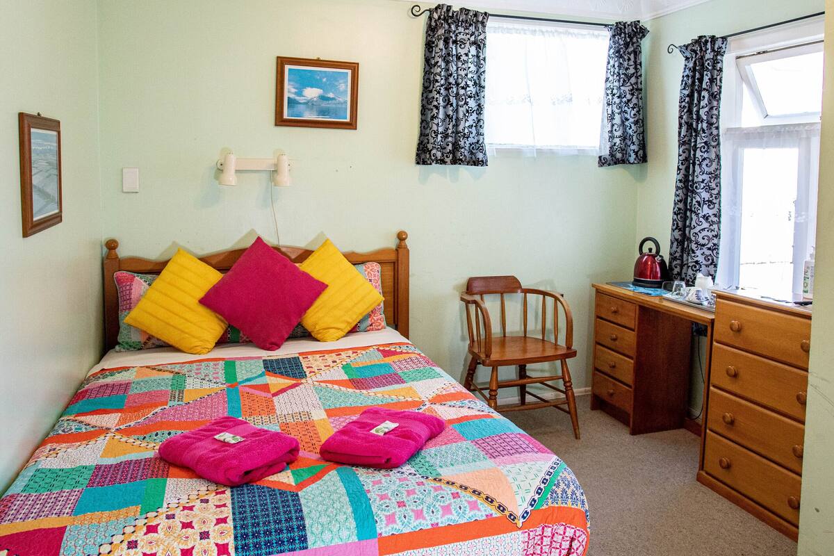 Une chambre à coucher avec un lit, un bureau, une chaise et une fenêtre avec des rideaux.