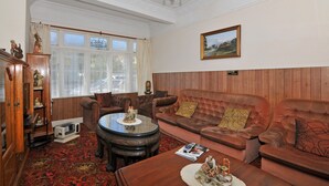 Een klassieke kamer met een houten paneelwand, een bruine leren bank, een ronde salontafel en een kroonluchter.