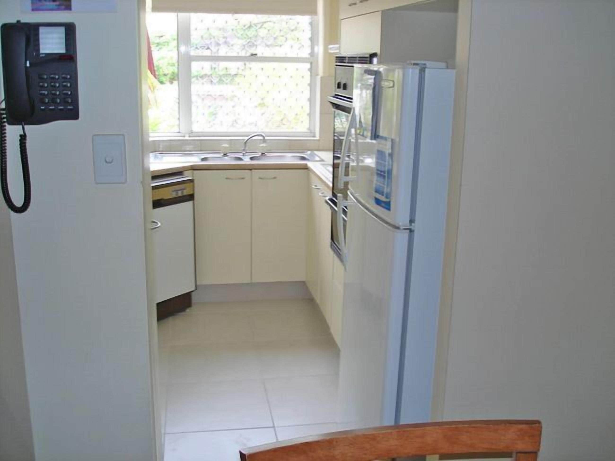 A compact kitchen with white cabinets, a built-in oven, a refrigerator, and a window with a view of greenery outside.