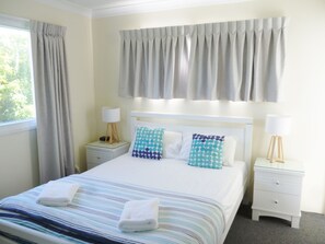 Une chambre d’hôtel avec un lit, deux tables de chevet, une fenêtre avec des rideaux et une vue sur la verdure.