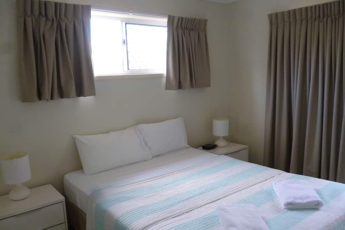 Une chambre d’hôtel avec un lit, deux tables de chevet, une fenêtre et des rideaux.