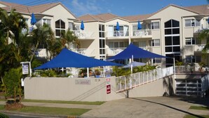 A hotel with multiple balconies, a gated entrance, and blue umbrellas. - Le Lavandou Holiday Apartments (Broadbeach)