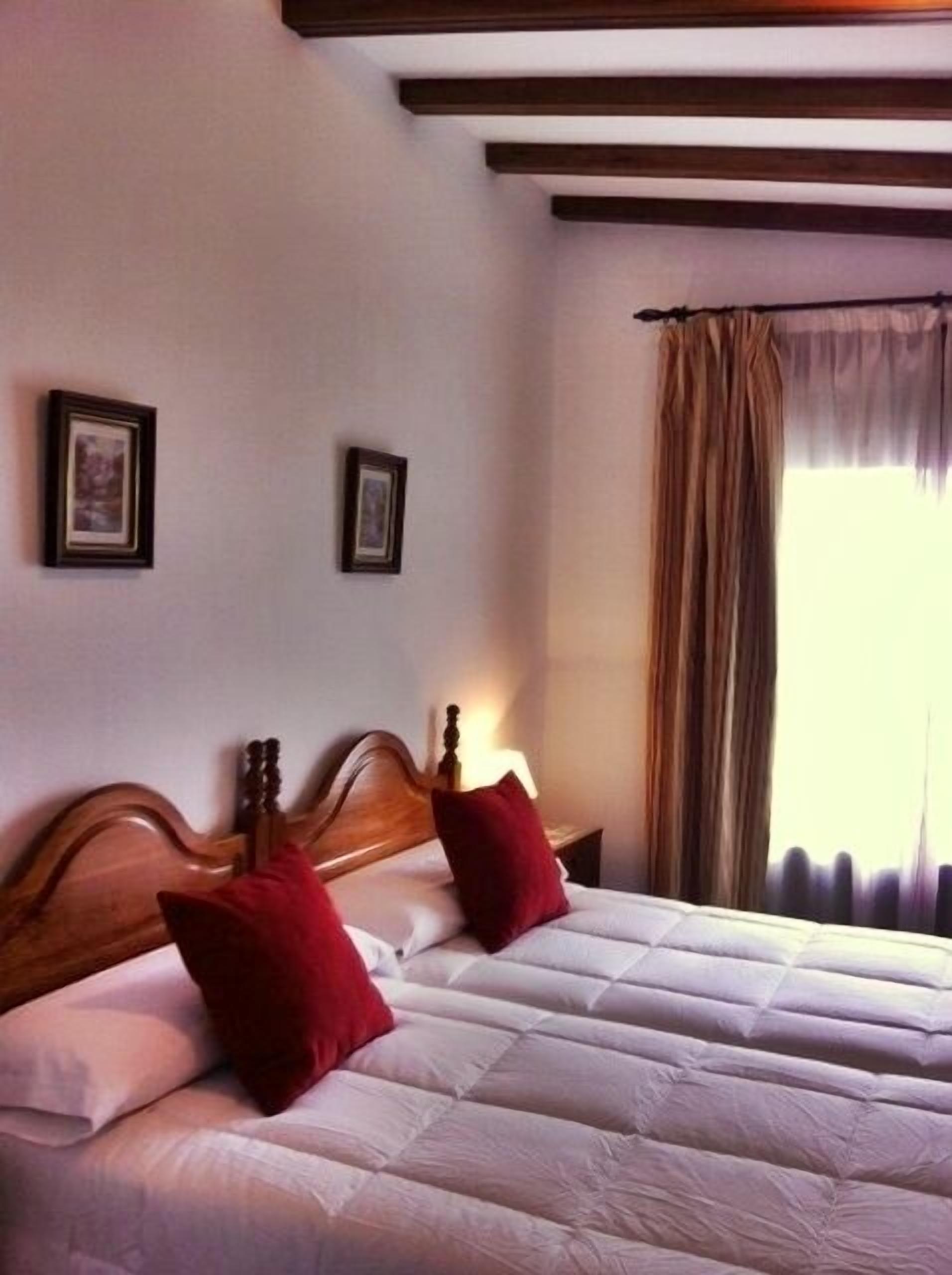 Una cama doble con cabecera de madera, dos almohadas rojas y un edredón blanco.