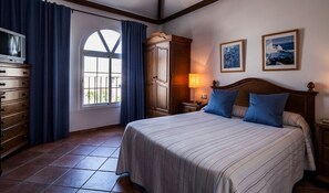 Un dormitorio con una cama grande, un armario, una cómoda, una ventana con cortinas y dos cuadros en la pared.