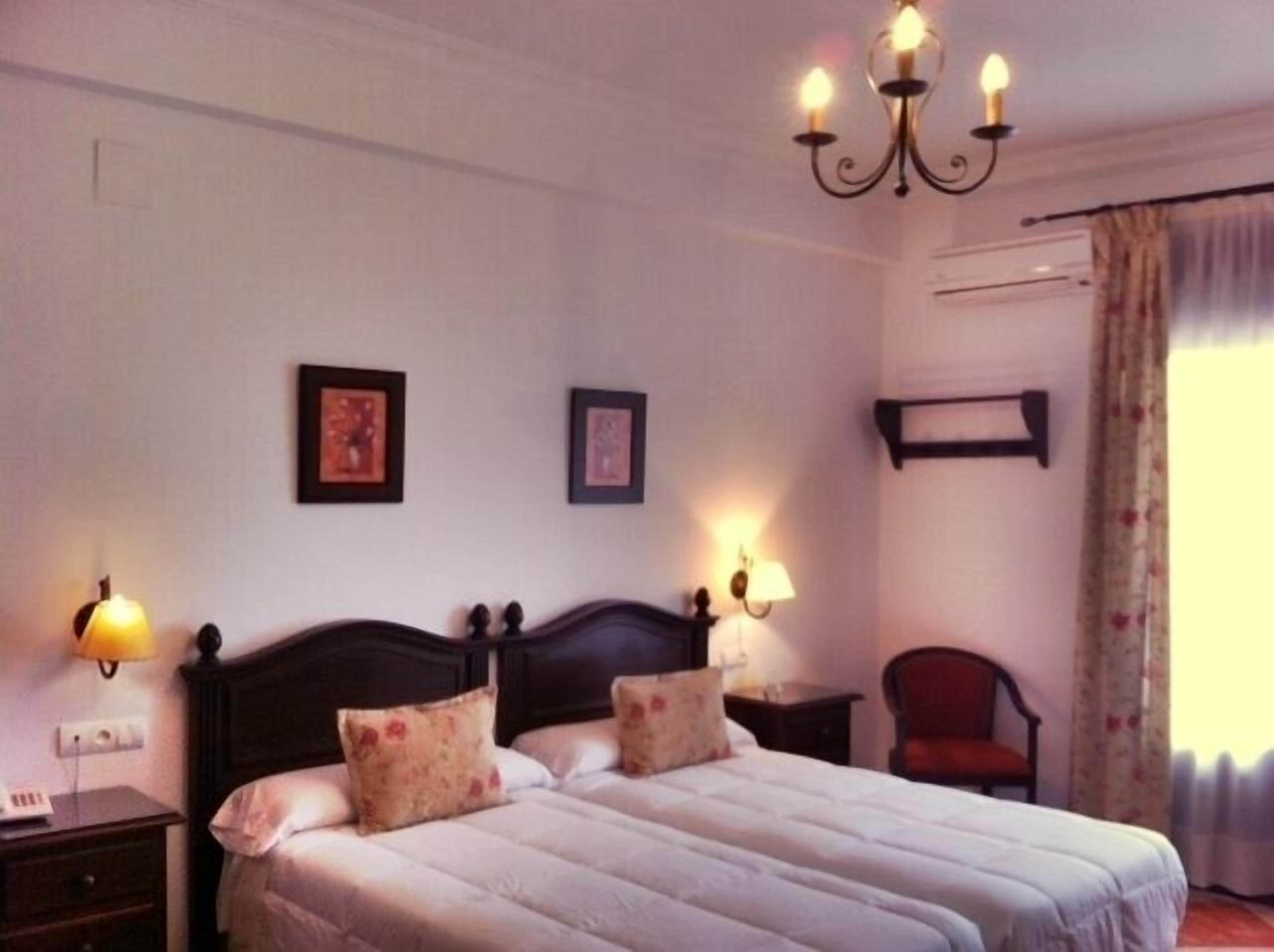 Un dormitorio con una cama doble, dos lámparas de noche, una araña y una silla.