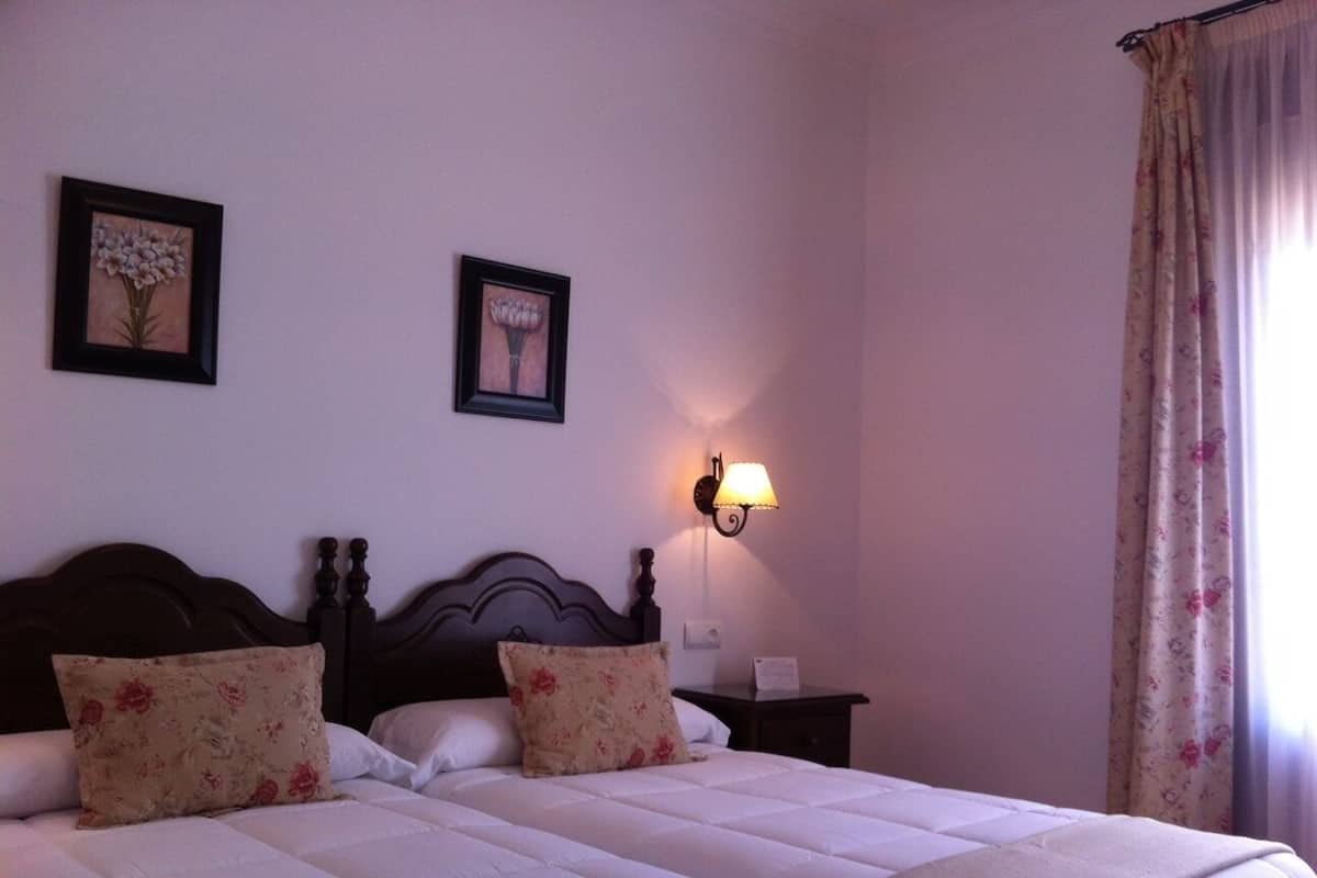 Un lit double avec des oreillers à motifs floraux, une table de chevet avec une lampe, et deux tableaux encadrés représentant des motifs floraux accrochés au mur.
