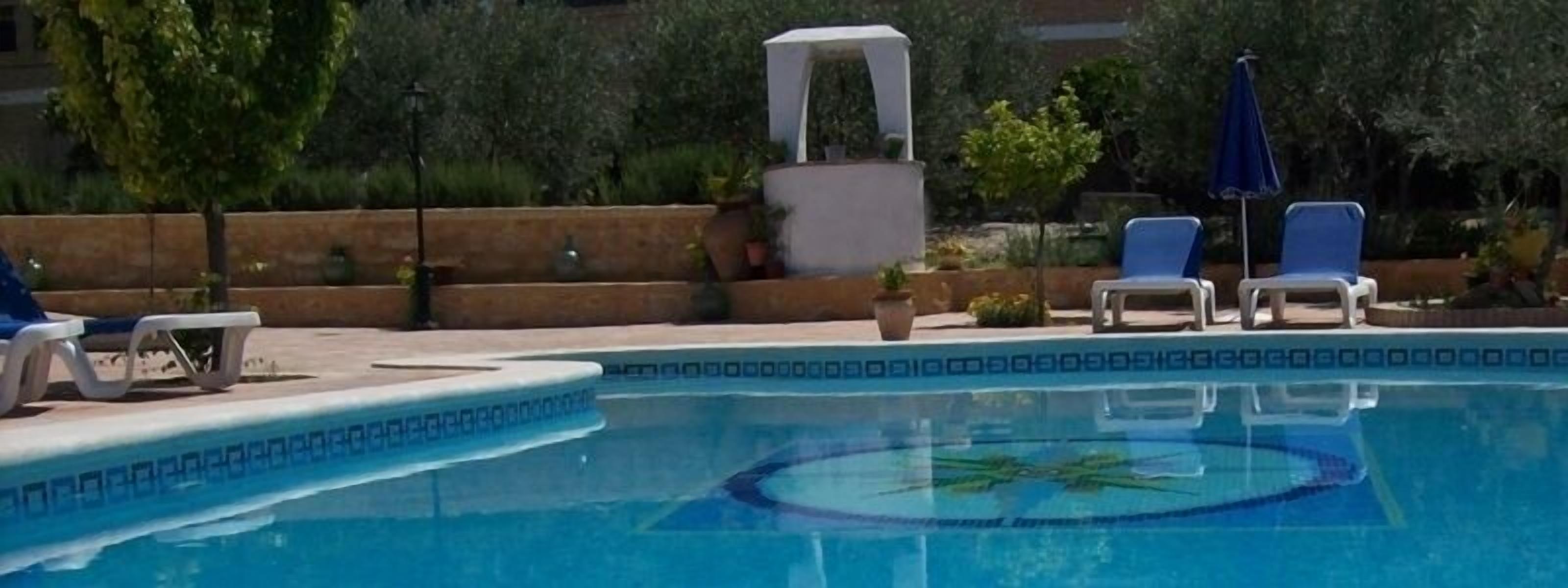 Una piscina con borde decorativo, sillas de descanso y un área de estar techada.