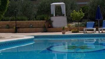 Una piscina con borde decorativo, sillas de descanso y un área de estar techada.