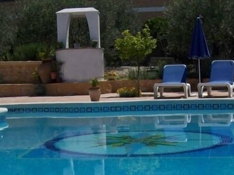 Una piscina con borde decorativo, sillas de descanso y un área de estar techada.