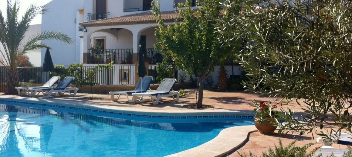 A swimming pool with lounge chairs and a building with balconies in the background.
