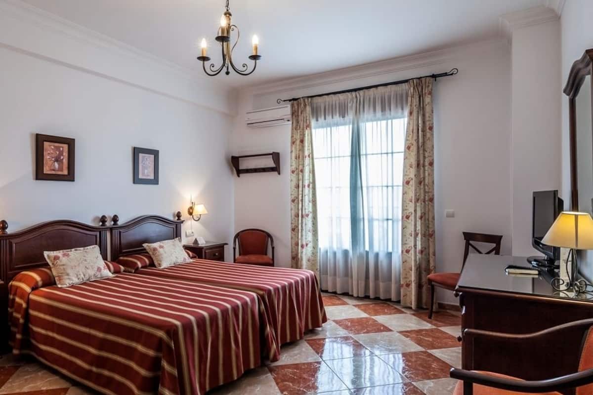 Une chambre d’hôtel avec un grand lit, un bureau avec une chaise, une télévision et un lustre.