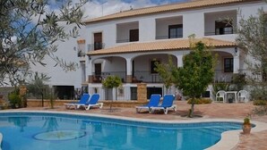 A two-story building with a swimming pool, blue lounge chairs, and a tiled patio area. - Hotel El Molino (Osuna)