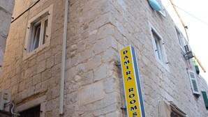 A stone building with a sign for "Damir Rooms" pointing to the right.
