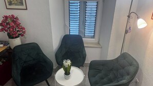 A small room with two dark green chairs, a white table, and a window with blinds.