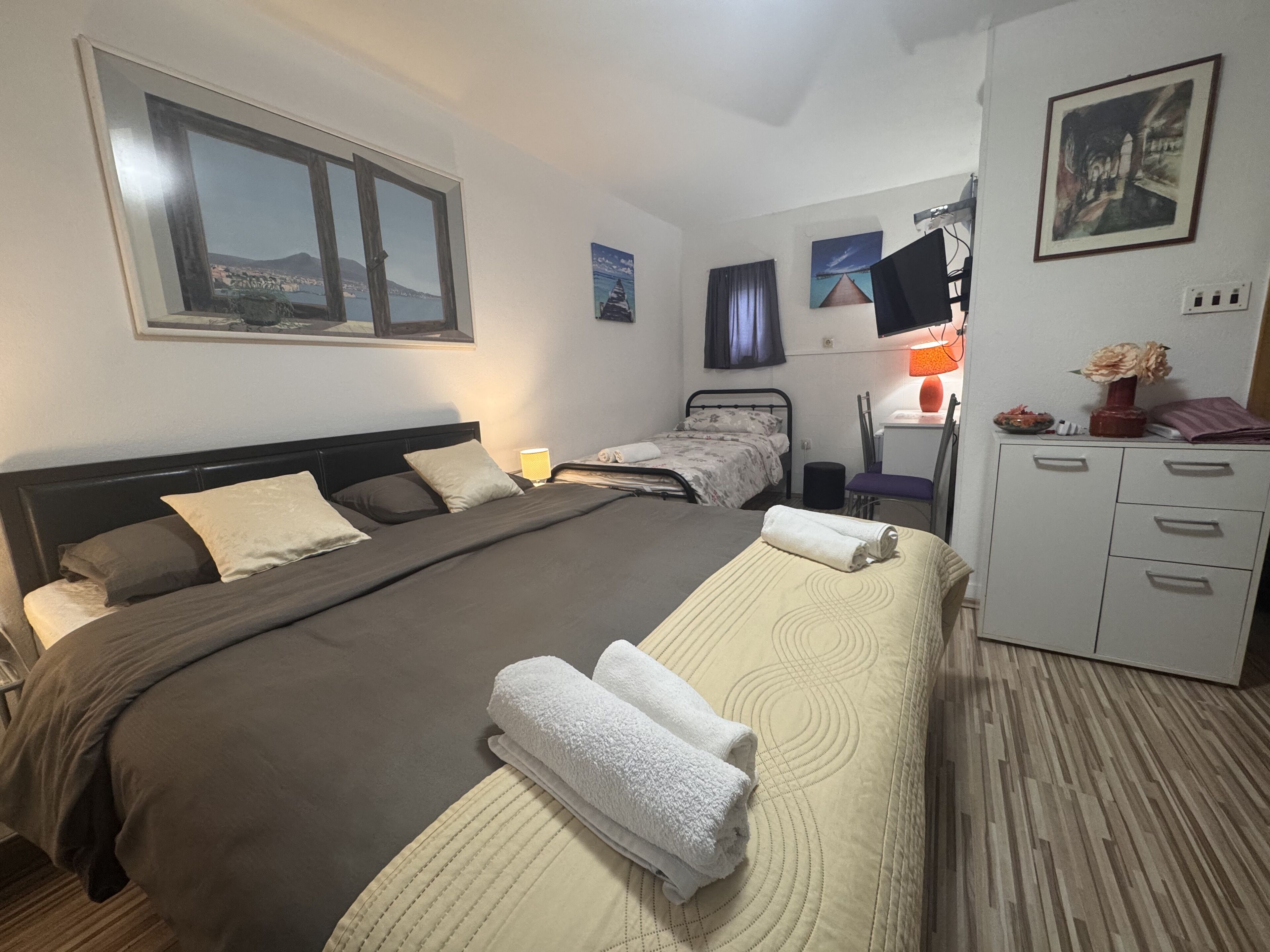 A hotel room with a large bed, a desk, a chair, and a wardrobe.