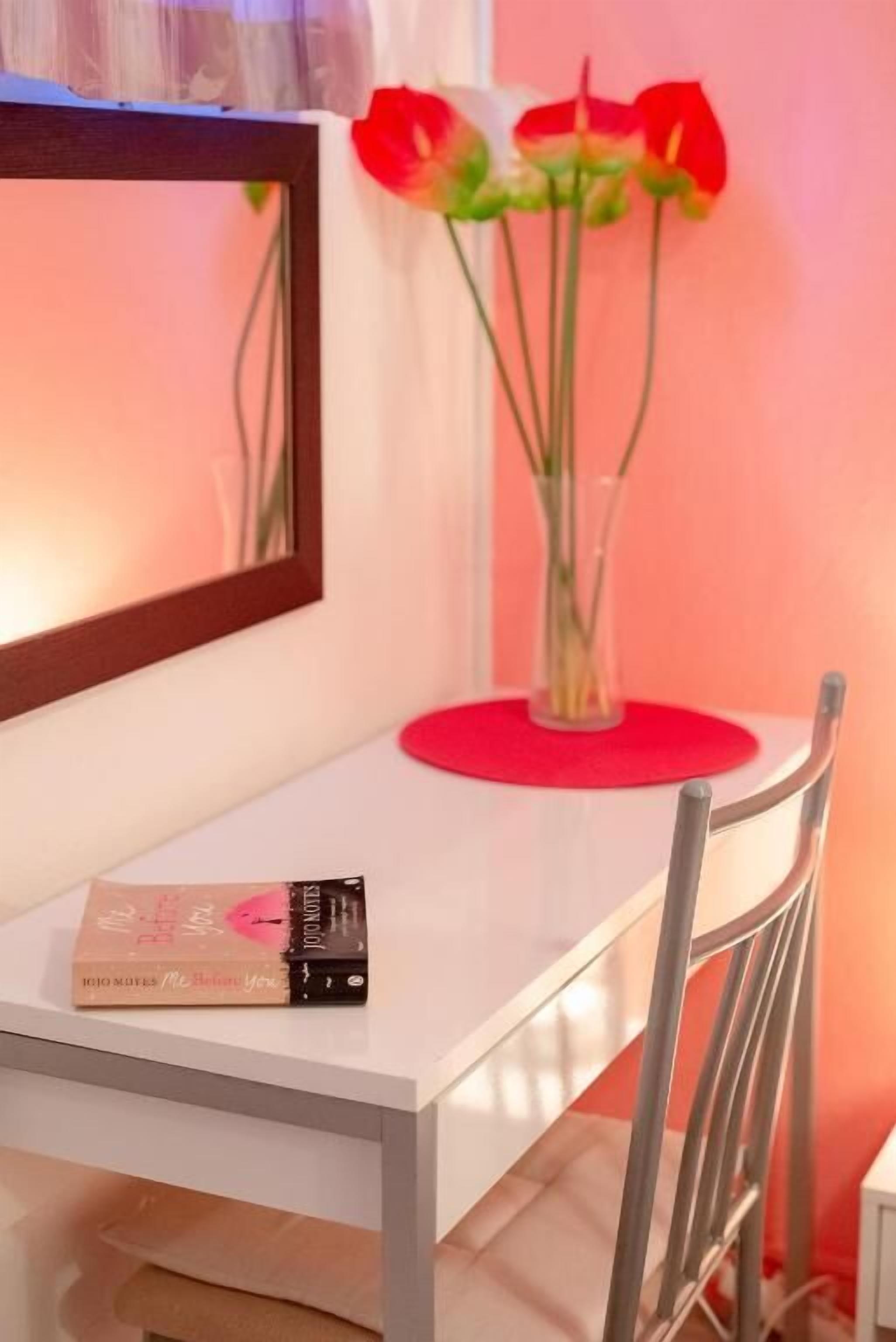 Ein weißer Tisch mit einer roten Vase voller roter Blumen, einem gerahmten Bild und einem Buch mit dem Titel 'My Best Friend'.