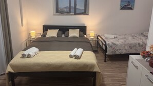 A bedroom with a large bed, two bedside tables with lamps, a small desk, and a window with a view of a landscape.